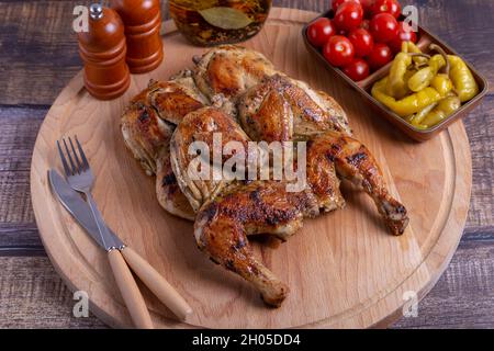 Tapaca (tabaca) Hühner mit Kirschtomaten und Pfefferoni auf einem Holzbrett. Traditionelles georgisches Gericht. Nahaufnahme. Stockfoto