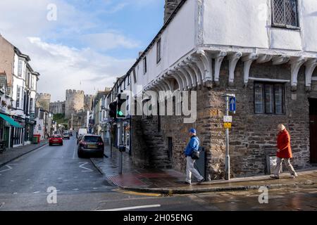 Am 4. Oktober 2021, in Conwy, Gwynedd, Wales, spazieren Sie ein Paar am Merchant's House aus dem 14. Jahrhundert in der Conwy High Street vorbei, wo das mittelalterliche Schloss die Stadt dominiert. Die Mauern wurden zwischen 1283 und 1287 nach der Gründung von Conwy durch Edward I. errichtet und sollten neben Conwy Castle ein integriertes Verteidigungssystem bilden. Die Mauern sind 1.3 km (0.81 mi) lang und umfassen 21 Türme und drei Torhäuser. Conwy ist eine ummauerte Marktstadt und Gemeinde an der Nordküste von Wales. Stockfoto