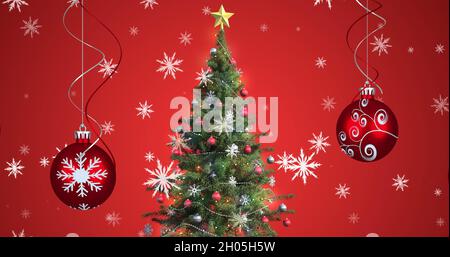 Bild von Schnee fällt über weihnachtskugeln und weihnachtsbaum auf rotem Hintergrund Stockfoto