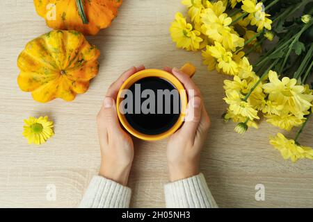 Weibliche Hände halten eine Tasse Kaffee auf einem hölzernen Hintergrund mit Kürbissen und Chrysanthemen. Stockfoto