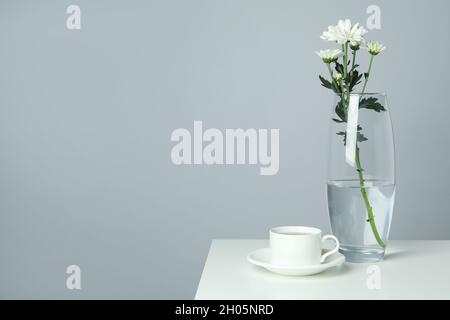 Vase mit Chrysanthemen und Tasse Kaffee auf weißem Tisch. Stockfoto