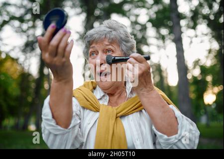 Hübsche ältere Frau macht Make-up im Sommerpark Stockfoto