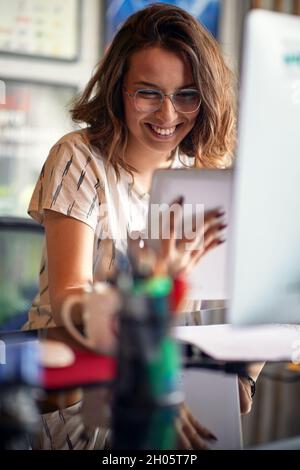 Die junge Frau benutzt ein Tablet, während sie in einer angenehmen Atmosphäre im Büro arbeitet Stockfoto