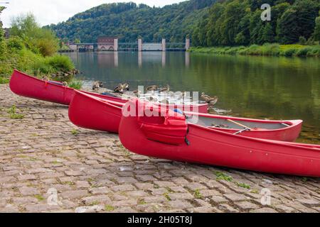 Drei rote Kanus mit nilgänsen und Schiff sperren sich im Hintergrund an einer Bucht für eine Flusswanderung als Freizeiterlebnis auf dem neckar in Süddeutschland ein Stockfoto