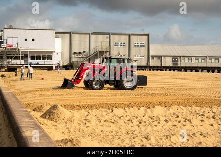 Leuchtend roter Baggerschlepper, der Sand von der Promenade weg bewegt und dabei den Sand vor dem Pier an der Küste von Lowestoft abflacht Stockfoto