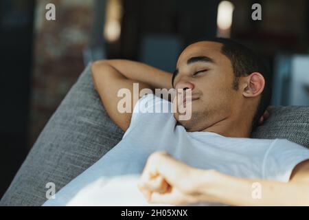 Erschöpfter junger schwarzer Mann, der ein ruhiges Nickerchen auf einem bequemen Sofa genießt, das sich mit geschlossenen Augen und einem zufriedenen Lächeln zurücklehnen kann Stockfoto