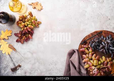 Weinflaschen mit Weintrauben und Weinläsern auf altem grauen Beton-Tischhintergrund mit Kopierraum. Rotwein mit Weinrebe. Weinkomposition auf Rusti Stockfoto