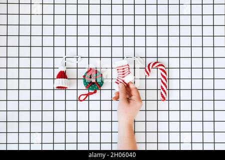 Weihnachten Strickspielzeug. Handgemachte DIY Häkelhut, Lollipop, Donut und Socke und weibliche Hand auf kariertem weißem Hintergrund. Weihnachten Strickmuster Stockfoto