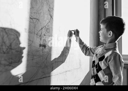 Das Kind zeichnet mit farbiger Kreide an die Wand. Der Junge beschäftigt sich zu Hause mit der Kreativität. Schwarzweiß-Foto Stockfoto