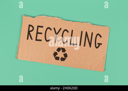 Recycling-Text und Pfeilsymbol auf Karton auf grünem Hintergrund Stockfoto