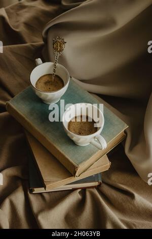Zwei Tassen Kaffee mit Milch mit einem Original-Löffel auf Büchern auf einem isolierten beigen Hintergrund. Stockfoto
