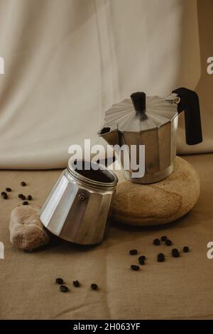 Kaffeekocher aus Metall auf einem Stein mit Kaffeebohnen und Kaffeepulver auf einem isolierten beigen Hintergrund. Stockfoto
