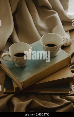 Nahaufnahme von zwei Kaffeetassen auf Büchern auf einem isolierten beigen Hintergrund. Stockfoto