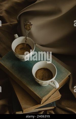 Zwei Kaffeetassen mit einem Original-Löffel auf Büchern auf einem isolierten beigen Hintergrund. Stockfoto