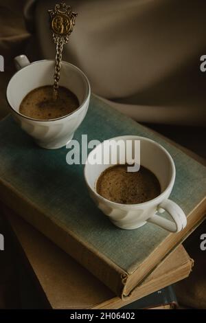Nahaufnahme von zwei Kaffeetassen mit einem Originallöffel auf Büchern auf einem isolierten beigen Hintergrund. Stockfoto
