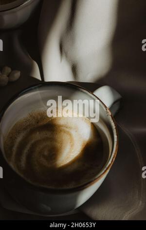 Still Life Tasse Kaffee, Bohnenkaffee auf Holzlöffel und Schale gemahlener Kaffee und Zucker auf beigem Hintergrund. Stillleben Kaffeefotografie. Stockfoto