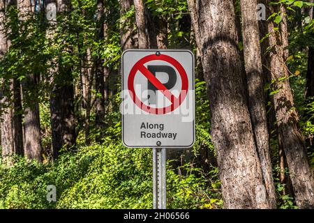 Ein Symbol ohne Parkplatzschild mit zusätzlichen Worten auf einer Straßenbeschilderung auf einem Pfosten im Park entlang der Nahaufnahme des Waldes Stockfoto