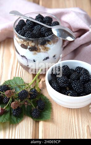 Nahaufnahme eines Käsekuchen mit Brombeeren im Glas und Brombeeren auf einem Holztisch. Stockfoto