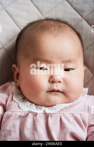 Portrait von asiatischen niedlichen neugeborenen Mädchen in schönen rosa Kleid auf dem Bett liegen Stockfoto