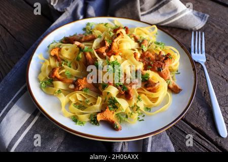 Tagliatelle-Pasta mit gebratenen in Butter gebackenen Pfifferlingen mit Knoblauch und fein gehackter Petersilie auf karierter Serviette auf rustikalem Hintergrund Stockfoto