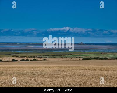Ein Fernblick über Felder von Lindisfarne (Holy Island) in Northumberland, England, Großbritannien. Aufgenommen im Sommer an einem sonnigen Tag mit blauen Wolken. Stockfoto
