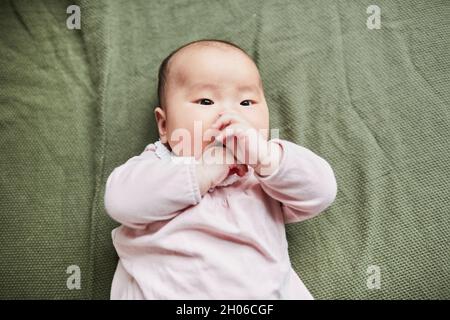 High-Angle-Ansicht der asiatischen niedlichen Baby auf dem Bett liegen und spielen mit ihren Fingern Stockfoto