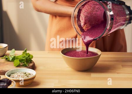 Hausfrau gießt frischen hausgemachten Obst-Smoothie in die Schüssel, die auf einem Holztisch steht Stockfoto