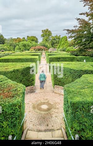 Ein Besucher auf dem von Hecken gesäumten Pfad zur Neptune's Grotto im Garten der Überraschungen im Burghley House, Stamford, England. Stockfoto