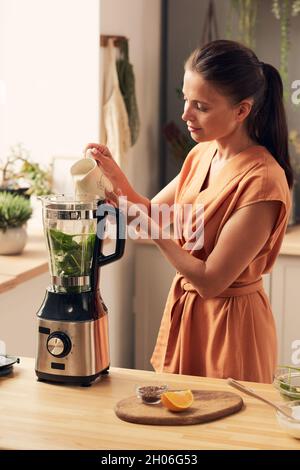 Junge Brünette Frau bereitet Spinat Smoothie am Tisch in der Küche Stockfoto