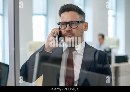 Reifer, eleganter Geschäftsmann oder Chef im Anzug, der im Büro auf dem Smartphone spricht Stockfoto