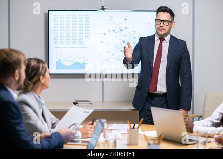 Seriöser Business Coach zeigt auf einen Mitarbeiter, während er seine Frage während der Präsentation beantwortet Stockfoto