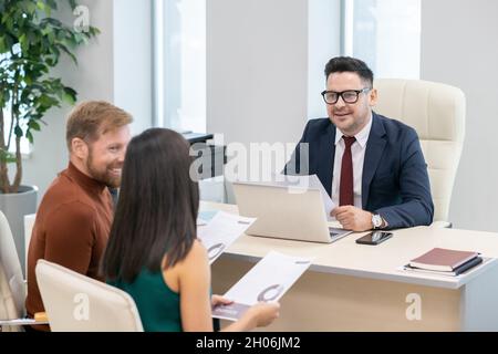 Erfolgreicher und erfahrener Auditor in der formalwear Beratung des jungen Paares in seinem Büro Stockfoto