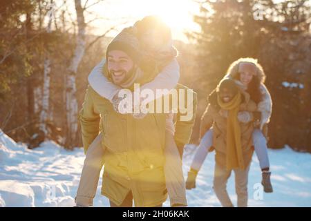 Zwei glückliche junge Paare in Winterkleidung, die am Winterwochenende am sonnigen Tag im Wald Spaß haben Stockfoto