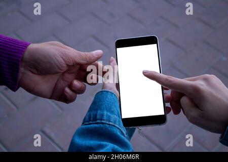 Frau, die ihrem Freund etwas auf ihrem Smartphone zeigt. Mockup-Bild einer weiblichen Hand mit Mobiltelefon mit leerem weißen Bildschirm. Stockfoto