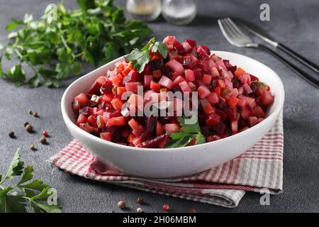 Traditionelle russische Salat-Vinaigrette aus Rüben, Kartoffeln, Karotten, Bohnen, Gurken, Zwiebeln und Pflanzenöl auf dunkelgrauem Hintergrund. Stockfoto