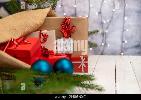 Jute Sack voller Weihnachtsgeschenke. Geschenke mit rotem, braunem und silbernem Papier mit rotem Band, Weihnachtsdekorationen und funkelnden Lichtern. Stockfoto