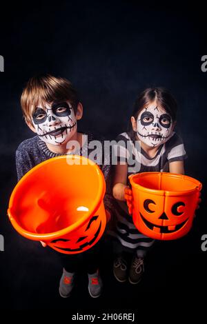 Zwei Kinder mit Totenkopf Make-up halten Kürbis Eimer an Halloween. Stockfoto