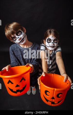 Zwei Kinder mit Totenkopf Make-up halten Kürbis Eimer an Halloween. Stockfoto