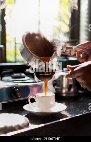 Frau gießt morgens Tee in die weiße Tasse. Sonnenlicht aus dem Fenster. Dampf kam aus den Utensilien und der Teetasse. Stockfoto