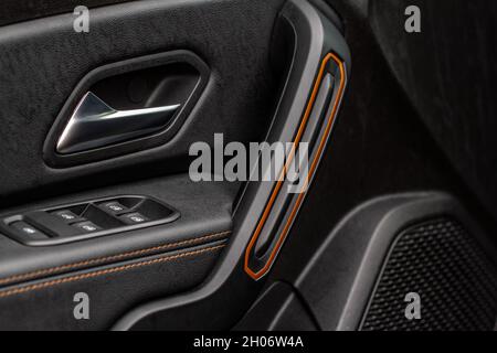 Türgriff für das Auto mit Fensterheber-Steuerung. Interieur aus dunklem Leder des modernen Autos. Dunkelschwarz und orange Auto Leder Falten Stich. Details zum Türhandl Stockfoto