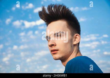 Außenportrait eines Teenagers, der mit im Wind wehenden Haaren gegen den Abendhimmel wegschaut Stockfoto