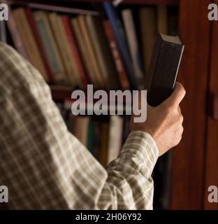 Nahaufnahme der Hand eines Mannes, der das Buch auf ein Holzregal in der Bibliothek legt Stockfoto