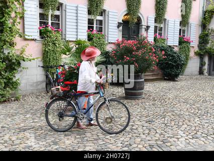 Bunter älterer Mann, der barfuß mit seinem dekorierten Fahrrad im Dorf Burkheim Deutschland läuft. Extravagant, stylisch, Stockfoto