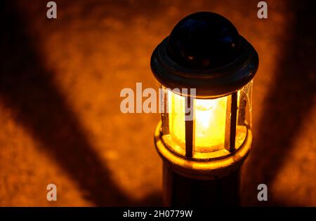 Lampe oder Licht in der Nacht in einem Park mit Schatten in einem kreisförmigen Muster. Das Licht beleuchtet einen steinigen Weg. Nahaufnahme der Lampe mit der Lampe Stockfoto