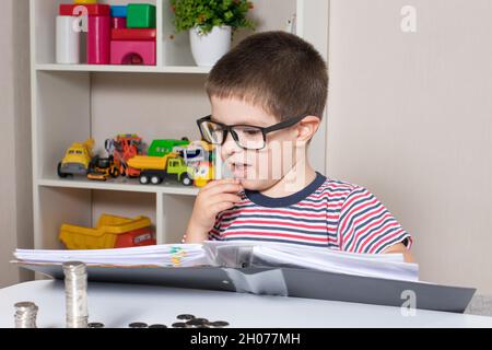 Ein junger Geschäftsmann im Vorschulalter denkt über Finanzen nach und plant, Geld und Münzen auszugeben. Stockfoto