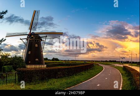 Alte holländische Windmühle an der Straße in Etten-Leur mit stürmischem Sonnenuntergangshimmel Stockfoto