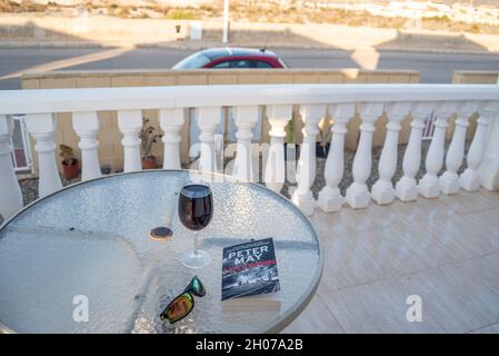 Reisekonzept nach COVID 19. Tisch vor einer spanischen Villa mit einem Glas Rotwein, Sonnenbrille und einem Buch mit dem Titel Lockdown Stockfoto