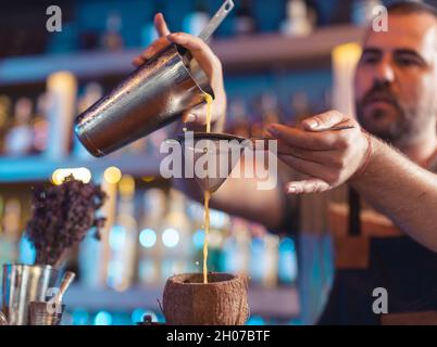 Barkeeper gießt Saft mit Sieb in Kokosnussschale in Bar Stockfoto