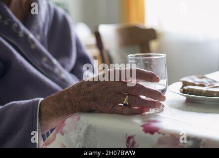 Nahaufnahme der Hand einer älteren Frau, die ein Glas Wasser am Tisch hält Stockfoto