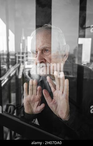 Einsamer alter Mann schaut aus dem Fenster und wartet. Das Konzept der Einsamkeit, des Alters, der Pandemieprobleme, der fehlenden Kommunikation. Quarantäneisolierung. Stockfoto